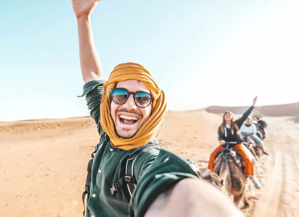 Happy tourist on a camel taking a selfie, waving arms in the air