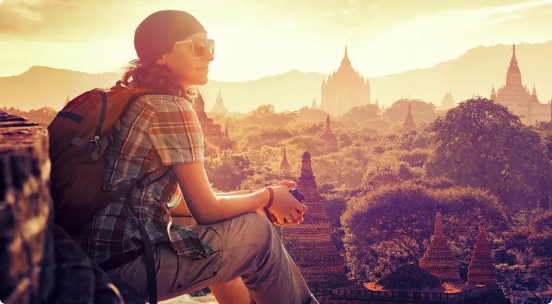 Female traveller seated, looking out over forest and temples at sunset