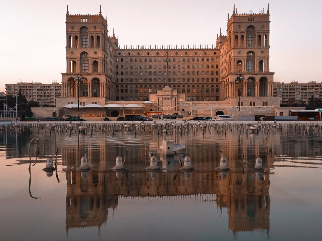 An impressively large ornate building with people gathering in a large square in front of it.