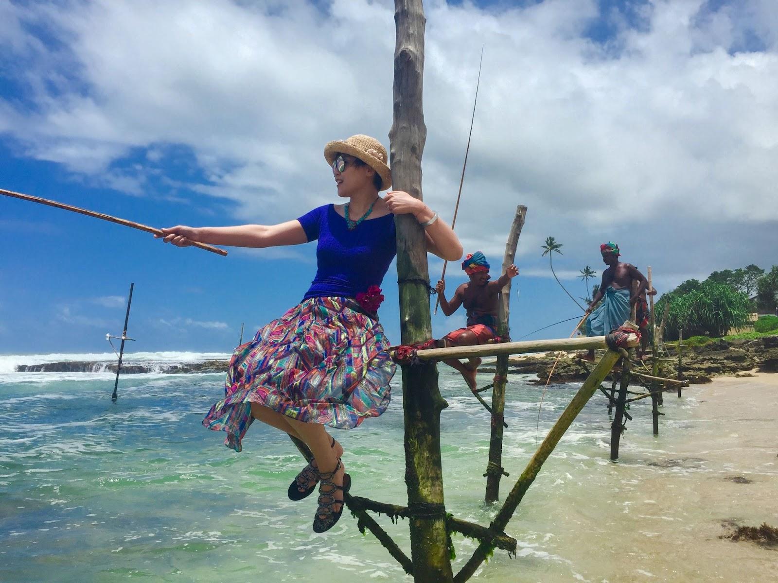 A lady stilt fishing on the beach of Sri Lanka alongside locals.