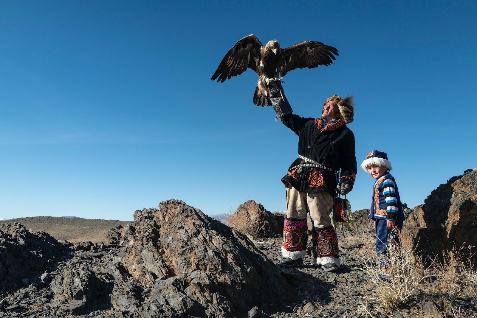 A Mongolian man flies a bird of prey with a child.