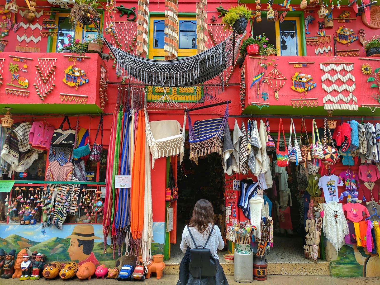 A women stands in front of a colourful shop selling hand bags in Colombia .