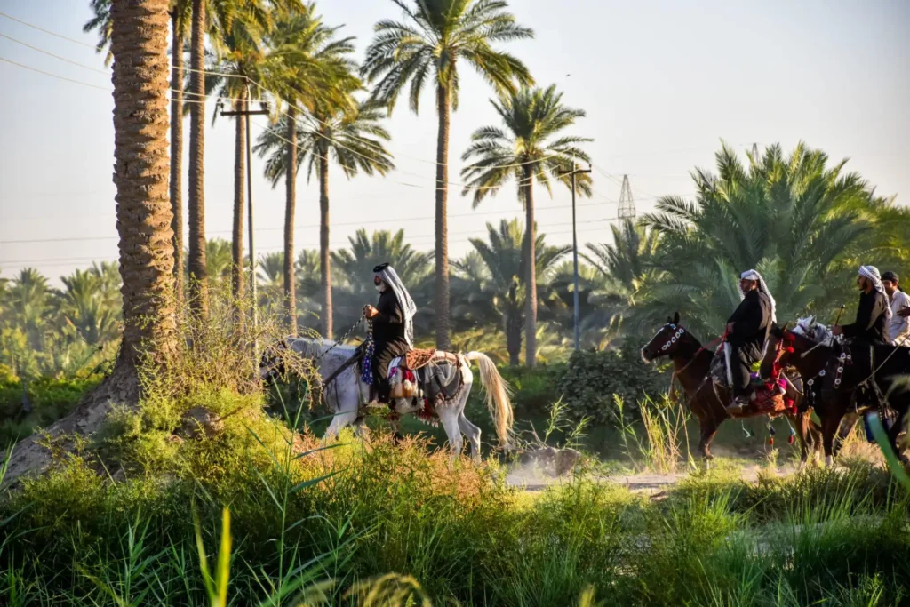 Iraqi men riding horses across a green grass field in Iraq.