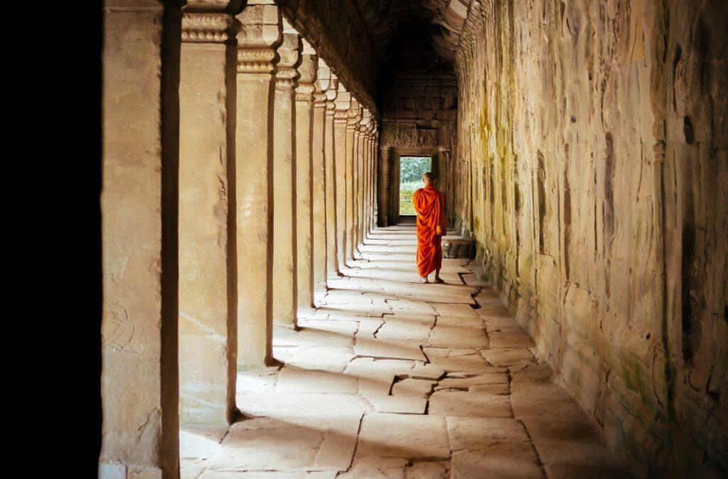 A monk pensively walks down the eves of a  Cambodian temple