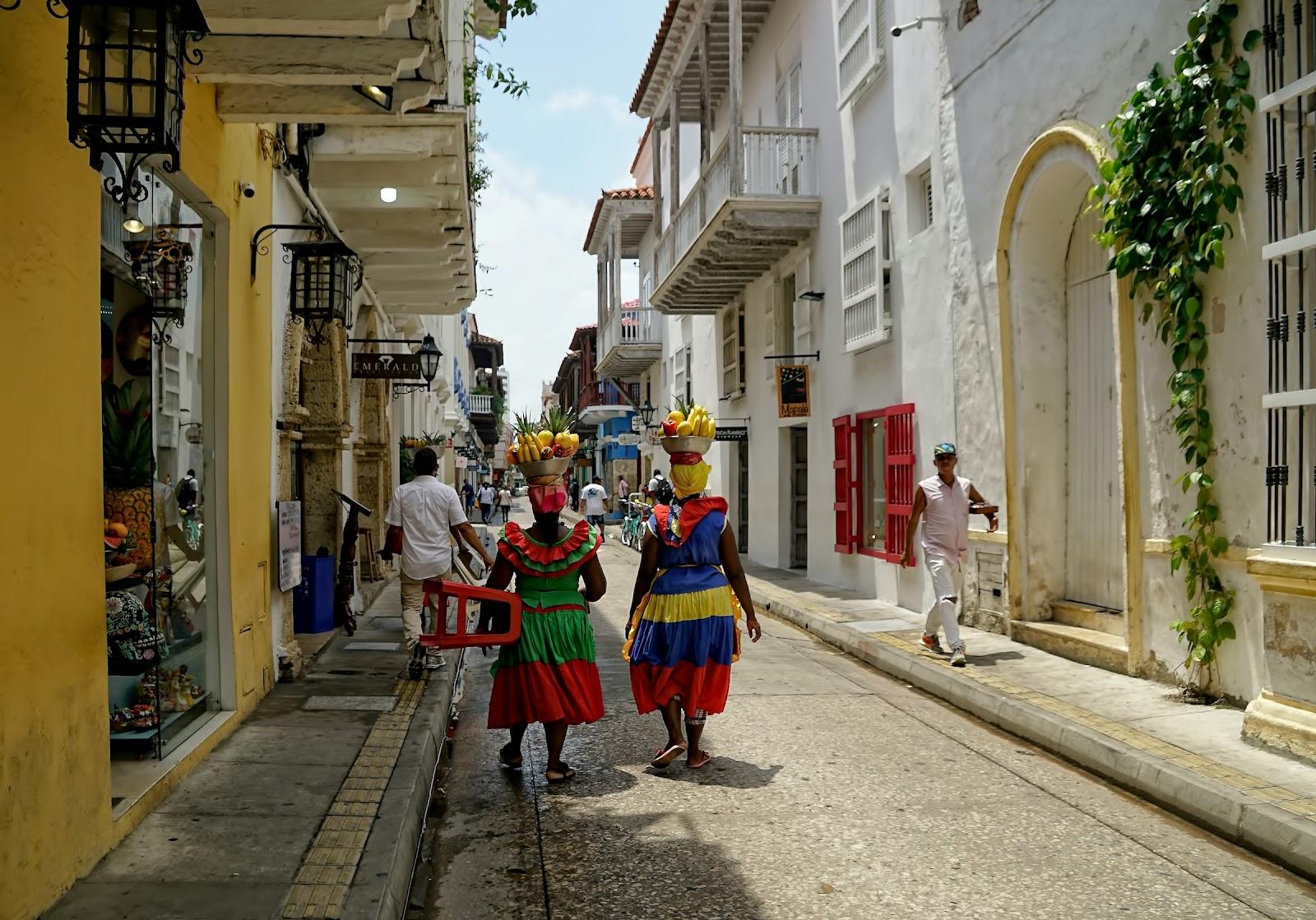 2 women in traditional Colombian clothes walking down a narrow street. 