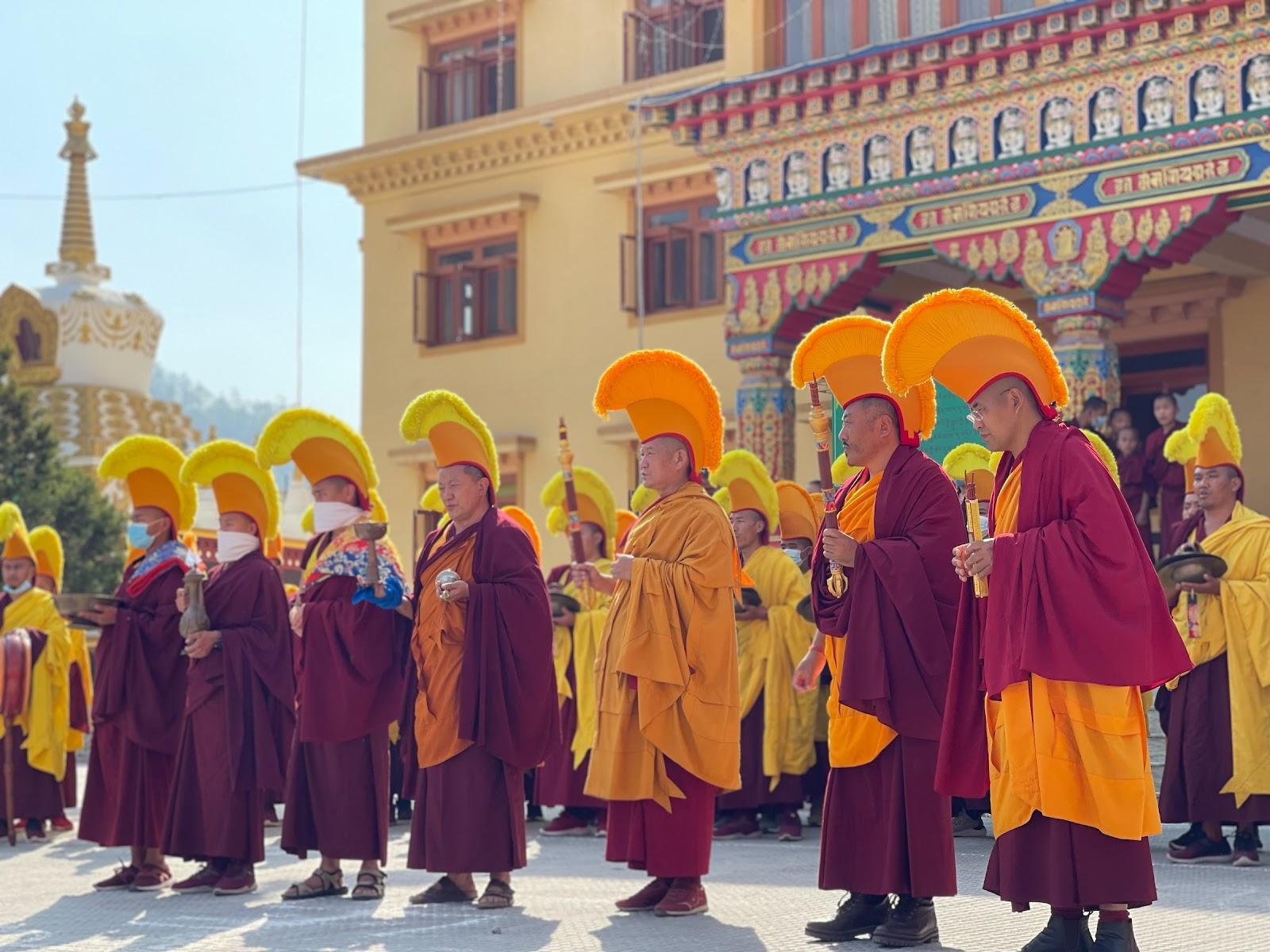 Buddhist monks wearing traditional garments and headdresses outside a temple in Nepal.