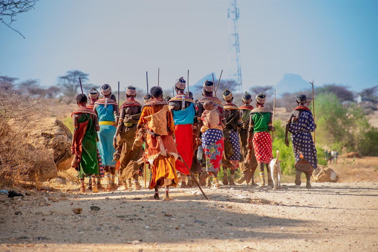 A group of Ugandan women walking, wearing colourful traditional clothing and carrying sticks.