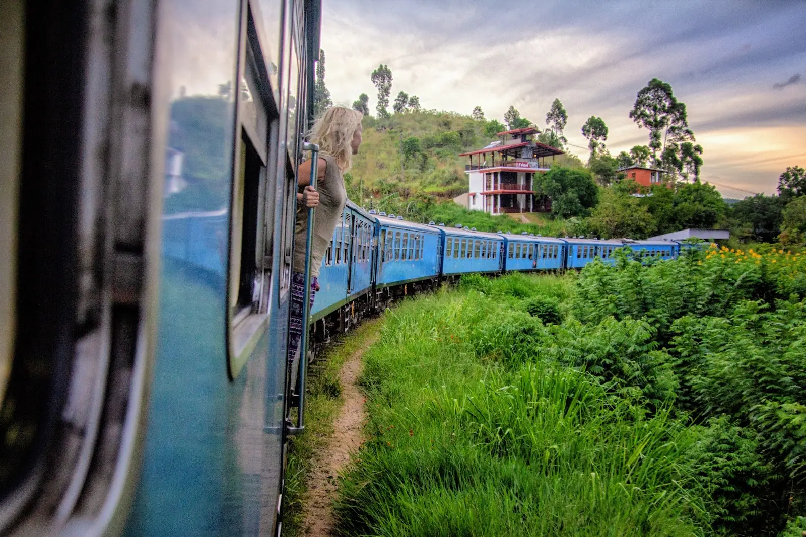 A women hangs out of a steam train admiring the view in Sri Lanka.