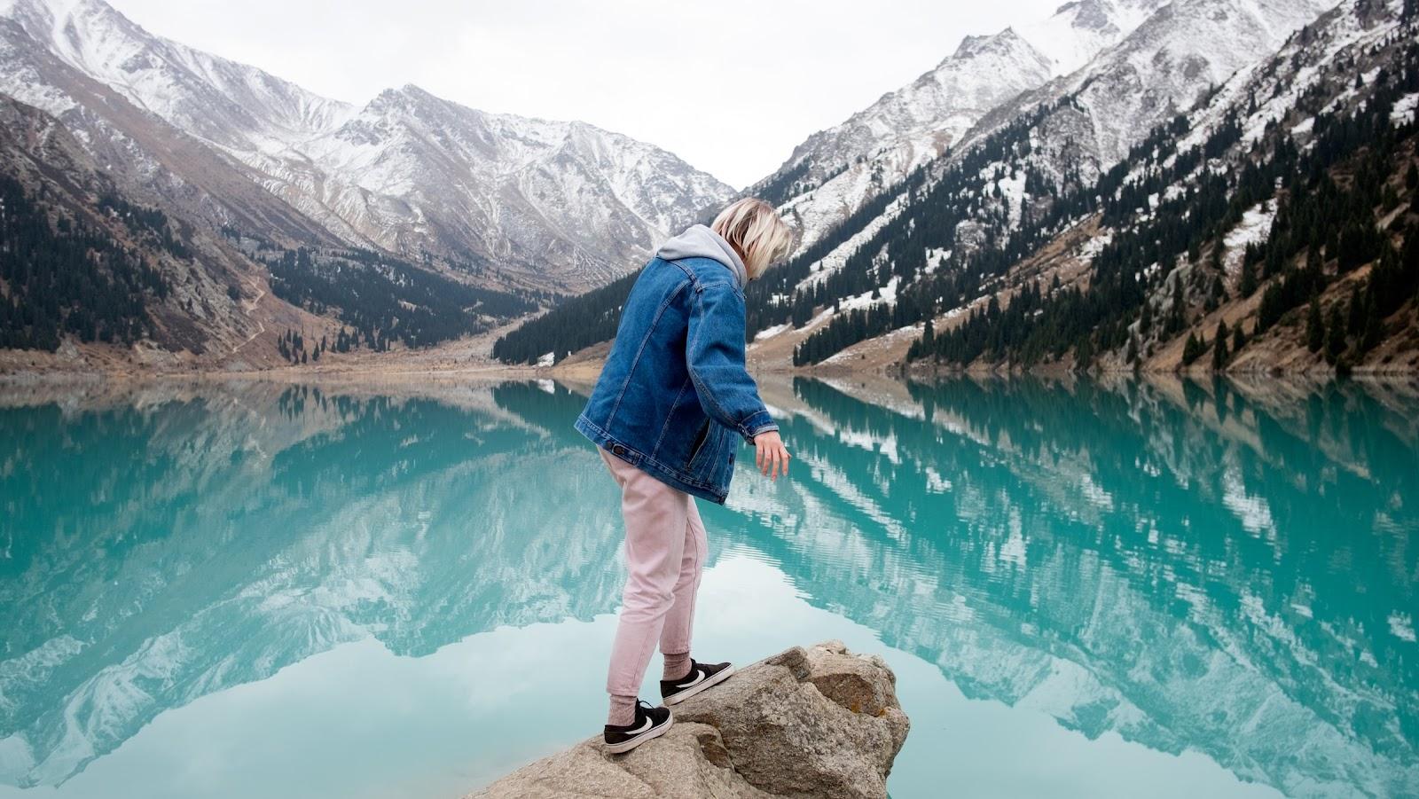 A women standing on a stone over looking a blue lake in Kazakhstan.
