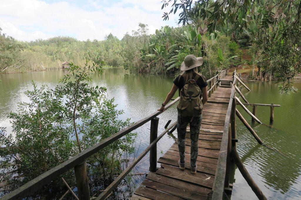 Woman walking on wooden bridge over a river in the forest - Madagascar