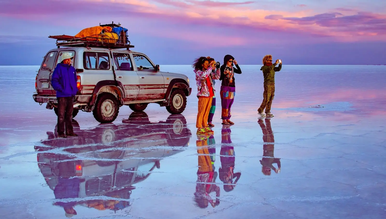 Group of tourists standing in front of a 4x4 taking pictures at sunset in Salar de Uyuni salt flats, Bolivia