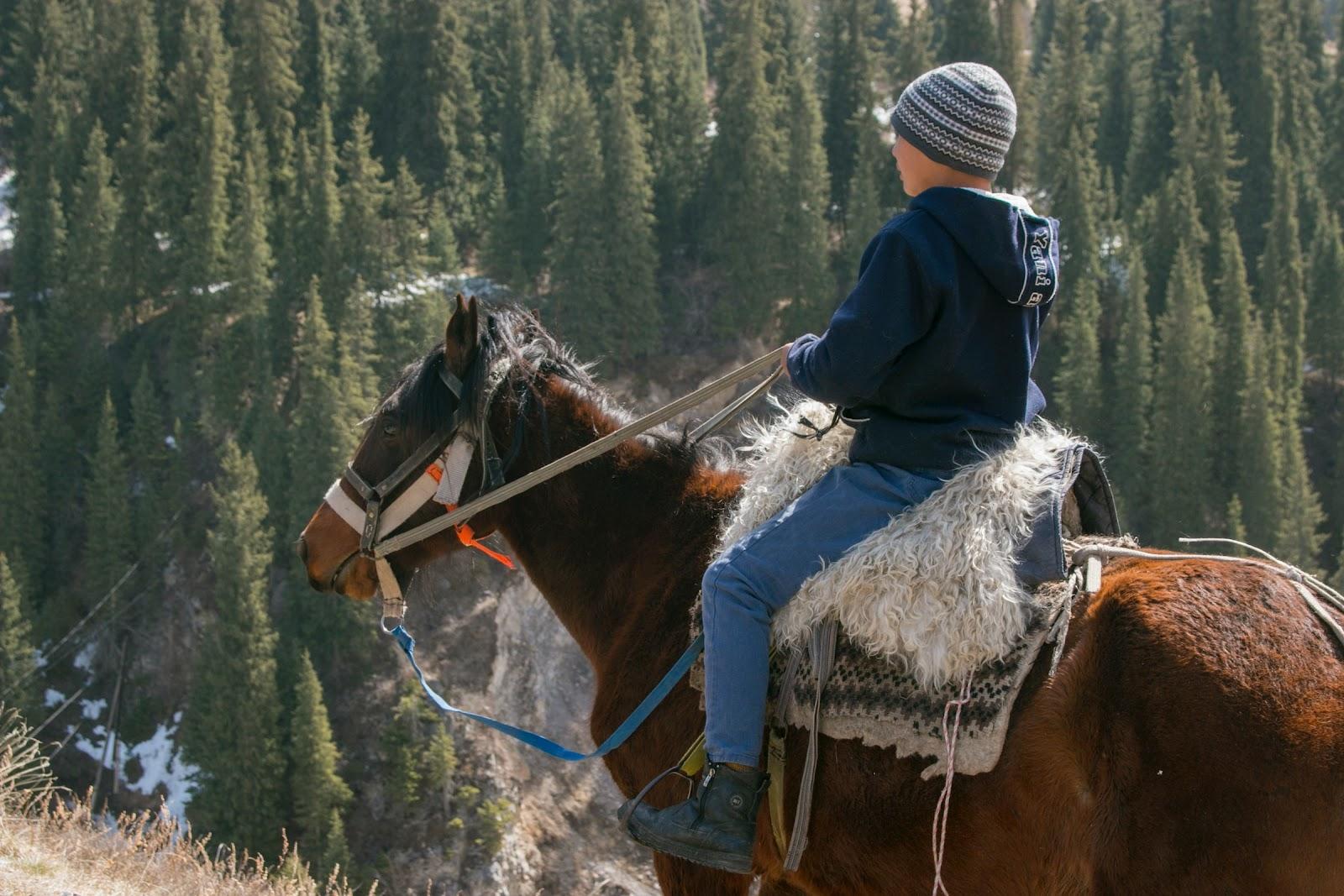 A boy riding a horse with a traditional Kazakhstan saddle. 