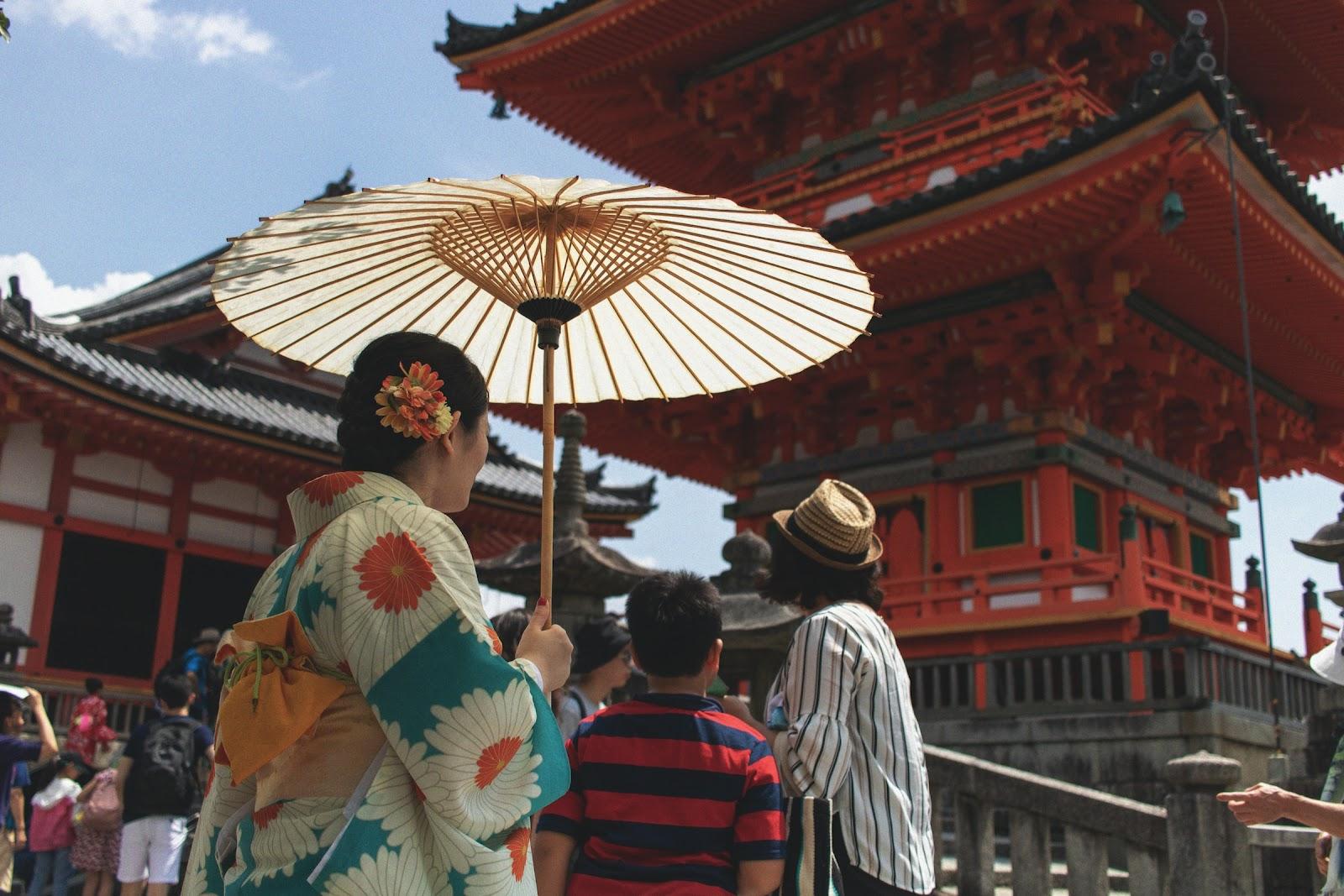 A women in traditional dress looking at a Japanese temple.