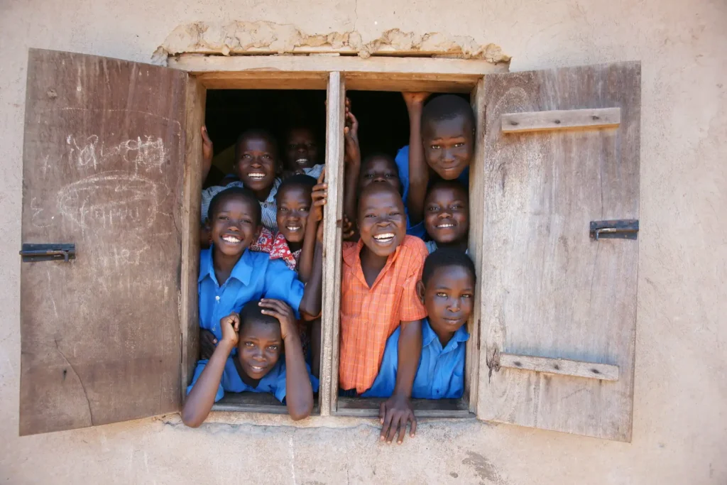Happy children look through a window in Uganda.