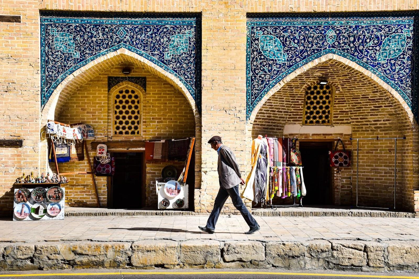 A Uzbekistani man walking past a building housing ceramics and fabric for sale.