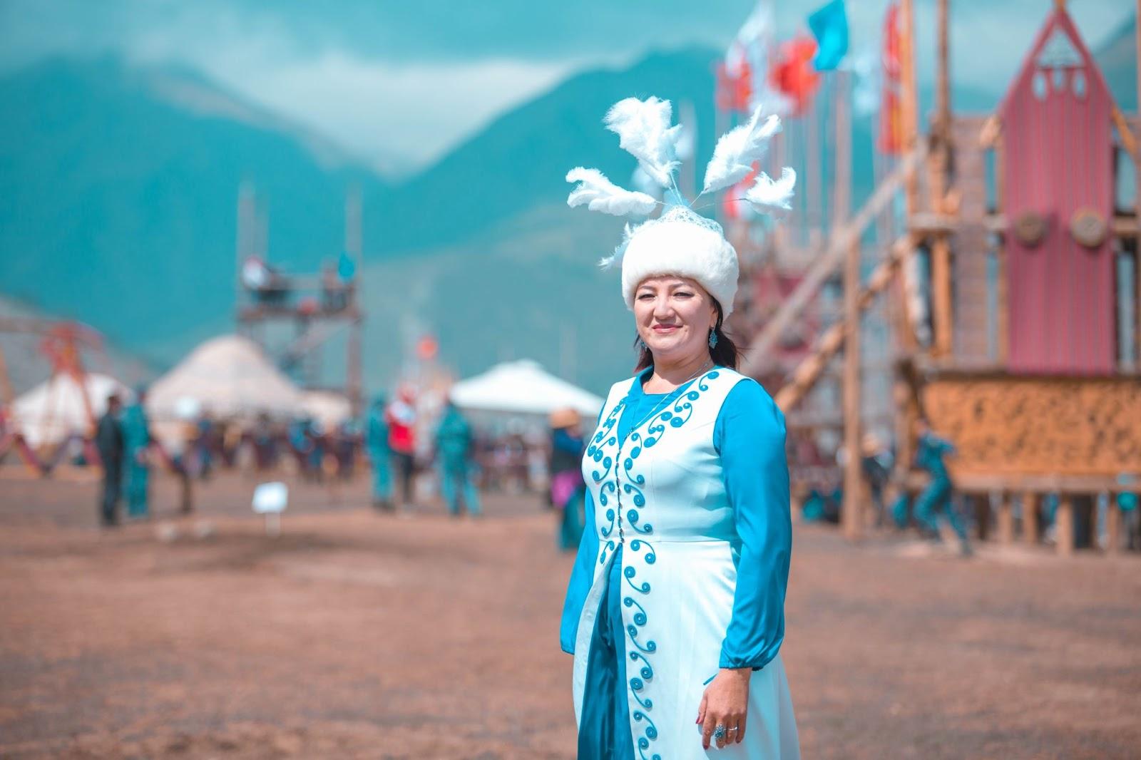 Kyrgyz woman in national dress standing near yurts during World Nomad Games