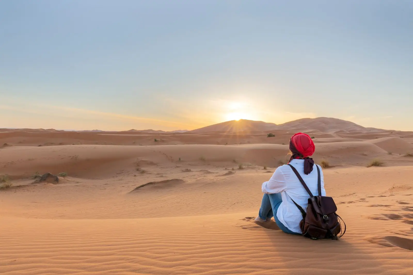 A women sits on a sand dune over looking the Tunisian desert.
