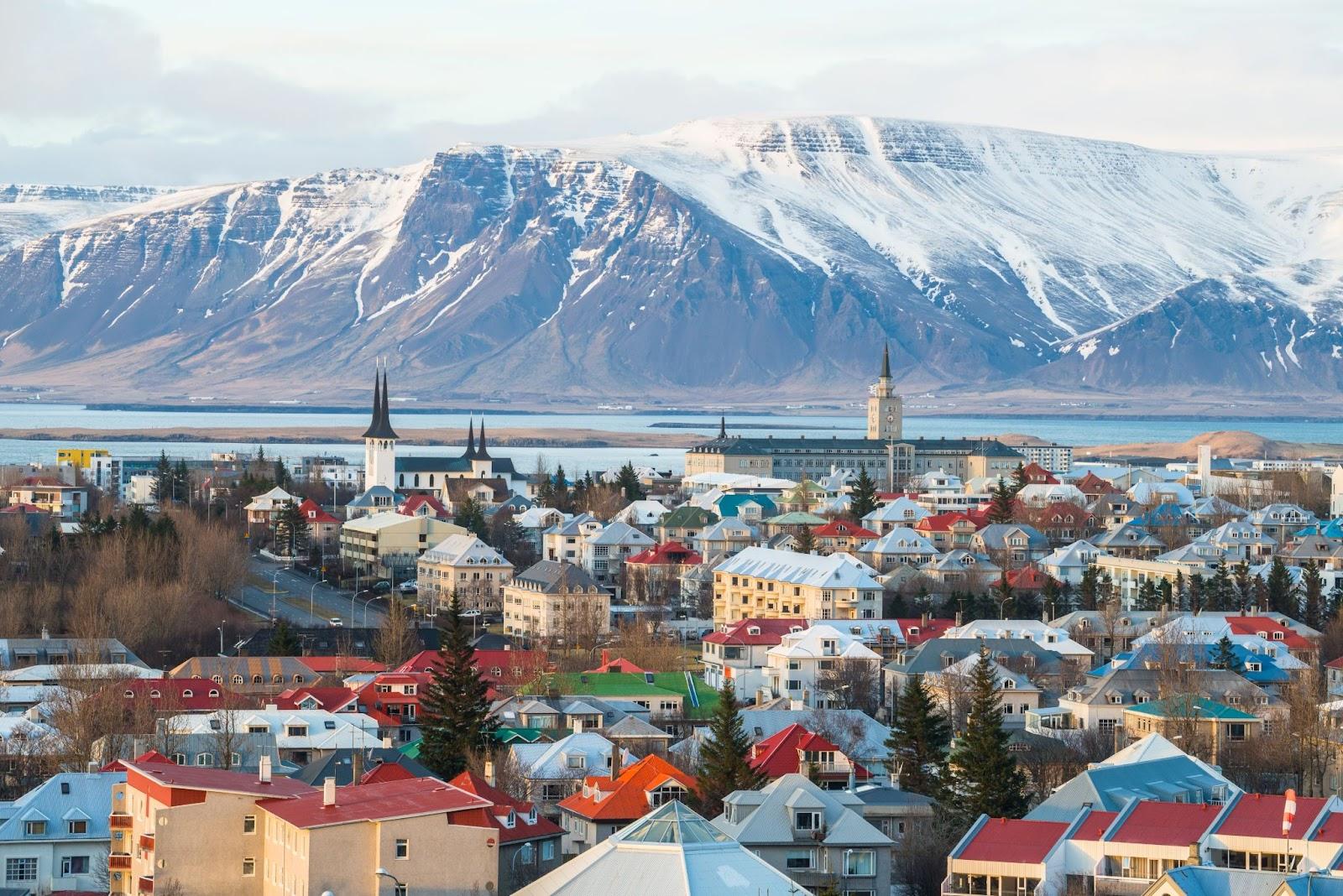 An Icelandic town overlooked by a snow covered mountain.