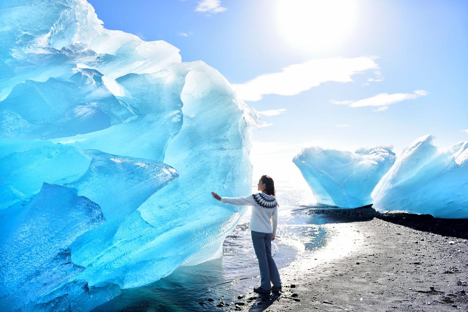 A women touching a blue iceberg in Iceland.