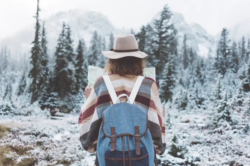 Woman with a backpack on holding a map looking out over a snowy landscape