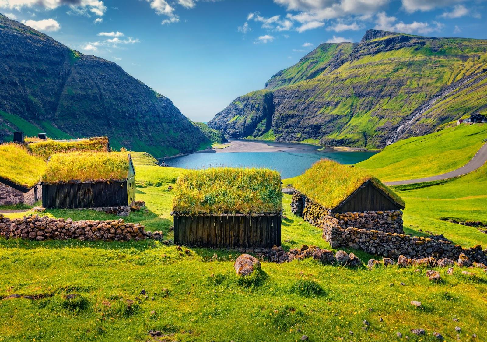Grass roofed houses over looking a Danish valley with a lake at the bottom.