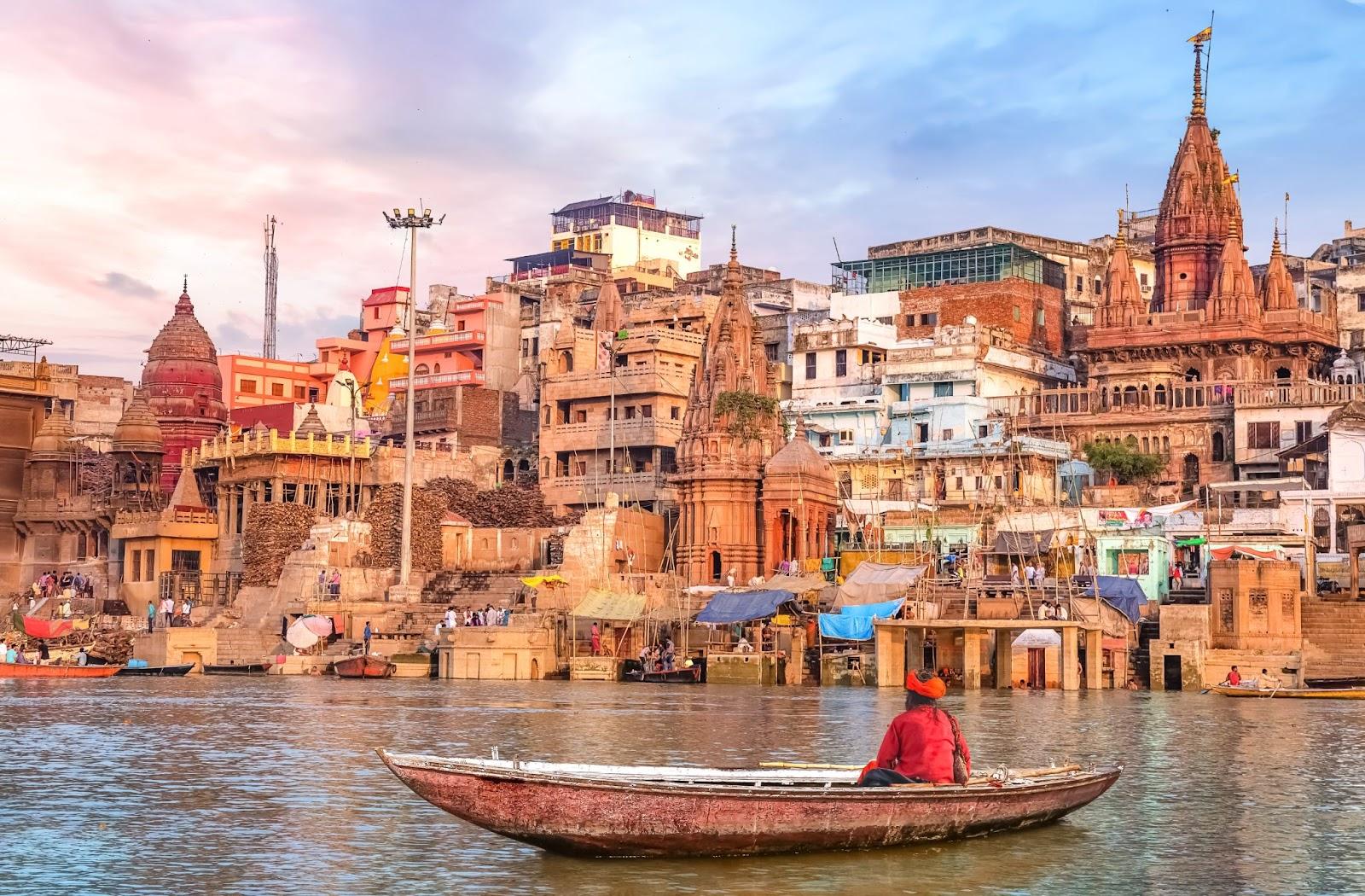 Ancient Varanasi city architecture at sunset with view of sadhu baba enjoying a boat ride on river Ganges