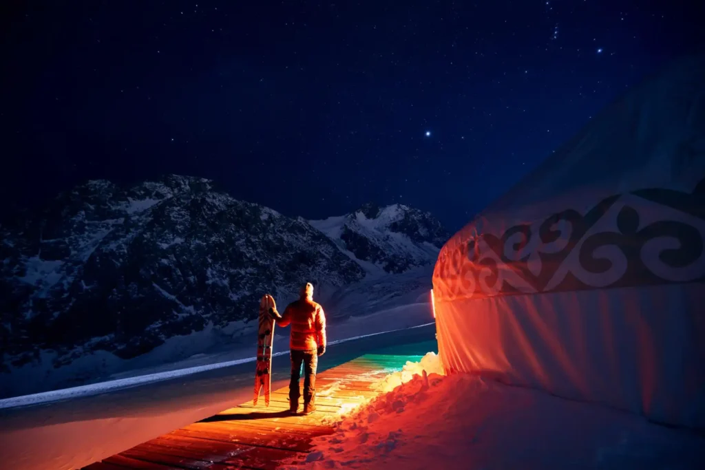 Man holding snow board near Yurt nomadic house complex at Ski resort Shymbulak in Almaty, Kazakhstan at night.