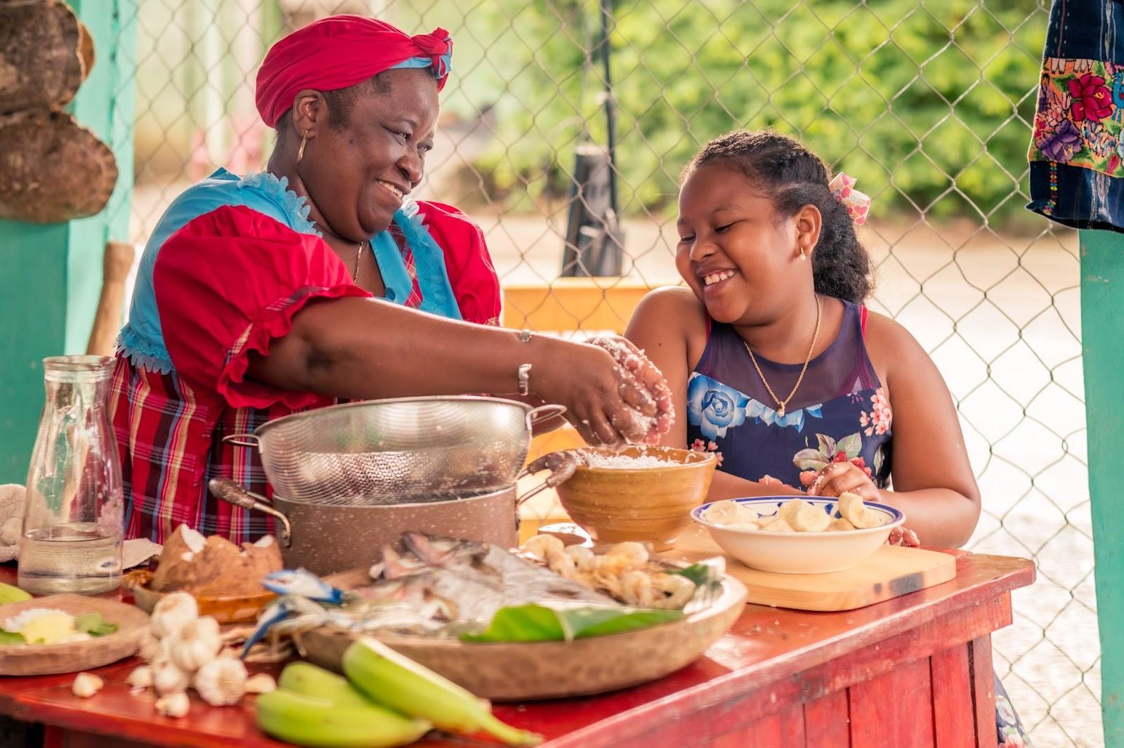 African-American mother teaches her little daughter how to cook Tapado. St Vincent East Caribbean