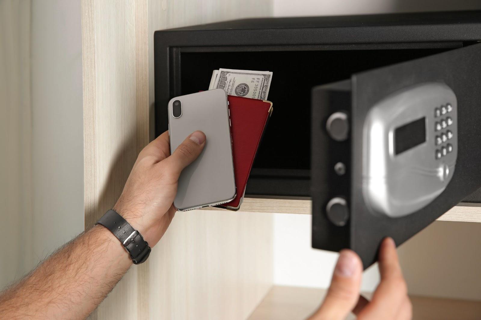 Man putting smartphone, passport and travel money into steel safe, closeup