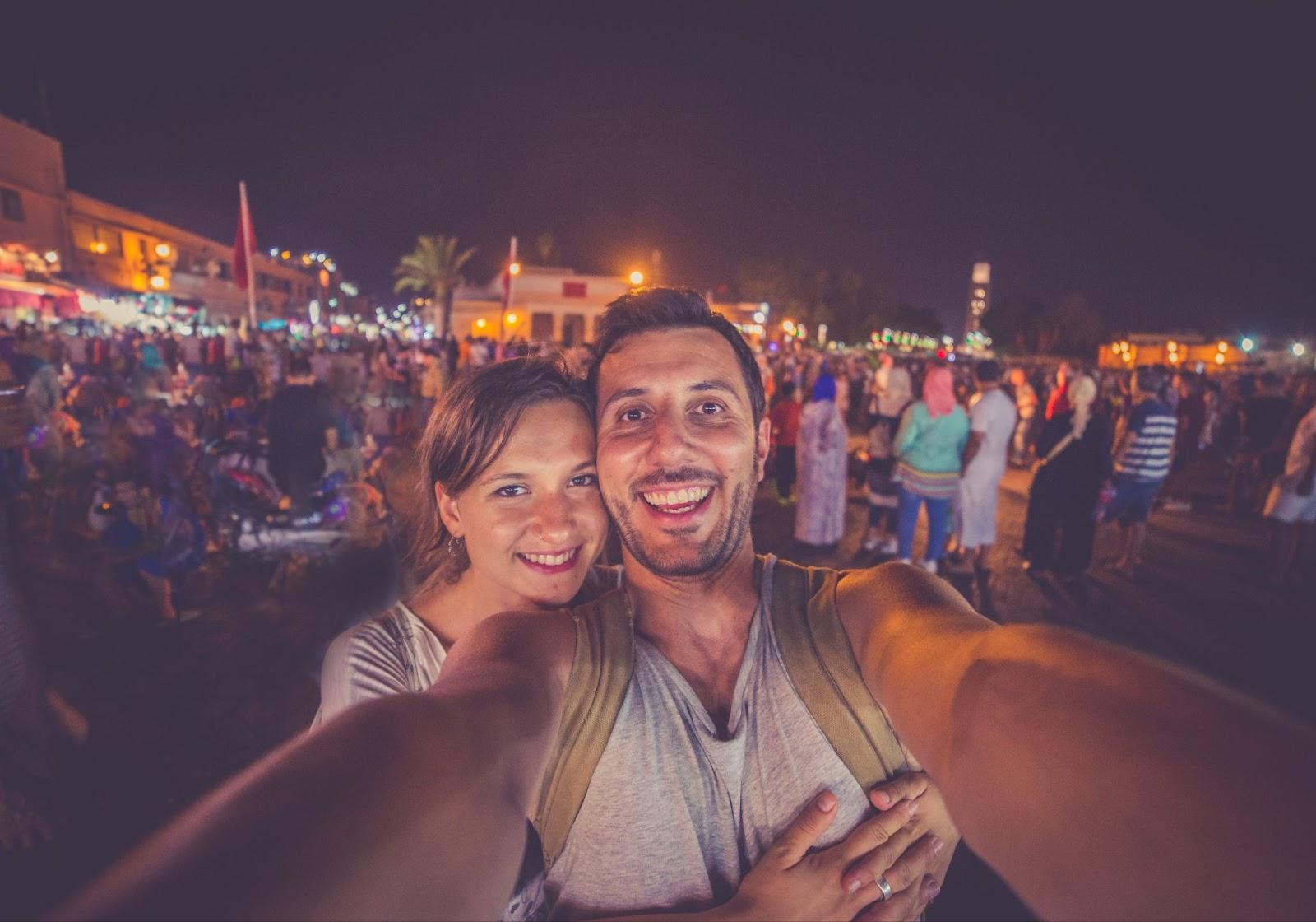 Happy tourists take selfie photo in the most important main square of Morocco Unesco site. Jamaa el-Fna market Marrakech at evening. - Valentines