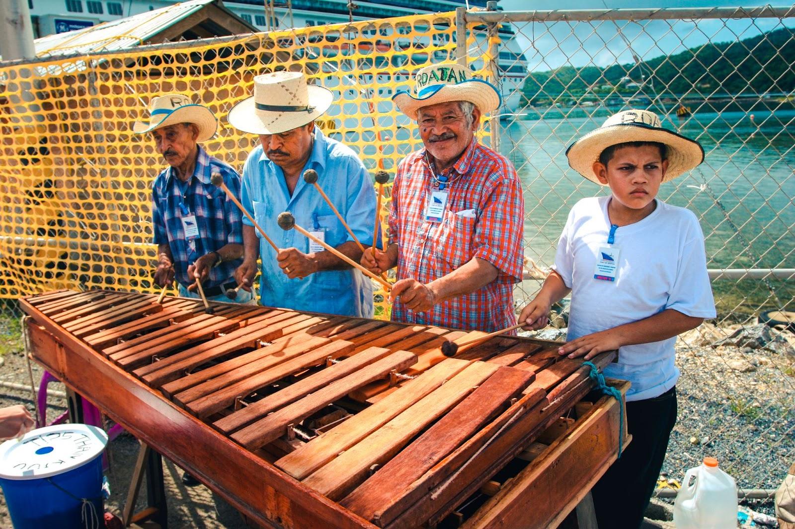 roup of local street musicians playing folk music on the wooden cymbals instrument. Dressed in the colorful shirts and straw hats on the head. Sunny day.