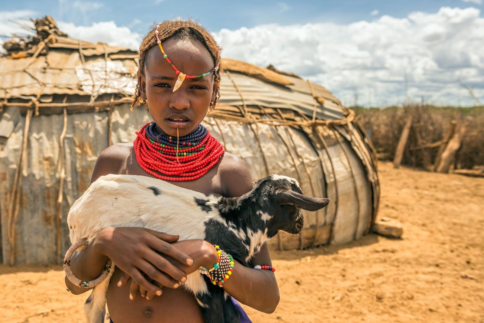 Girl from the Ethiopian tribe Dasanesh holding a goat in her village