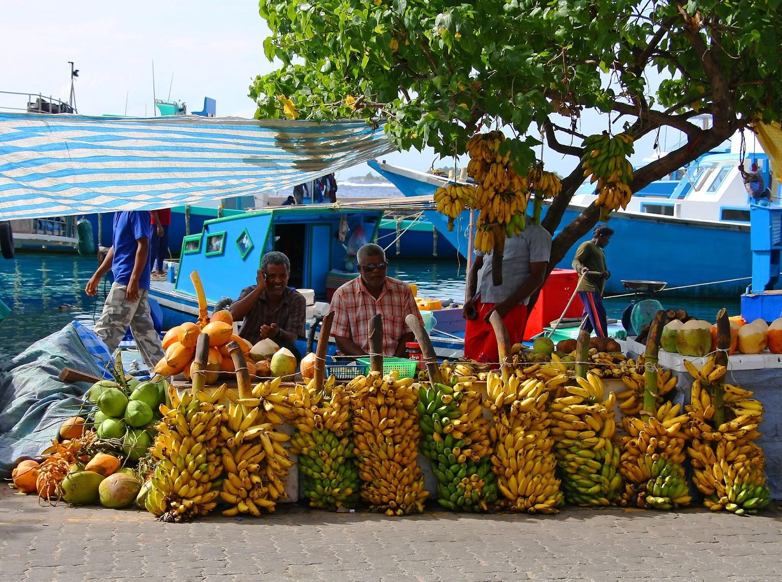 Three street vendors sit by bananas stall - Market situated on the harbor of Male - capital of Maldives