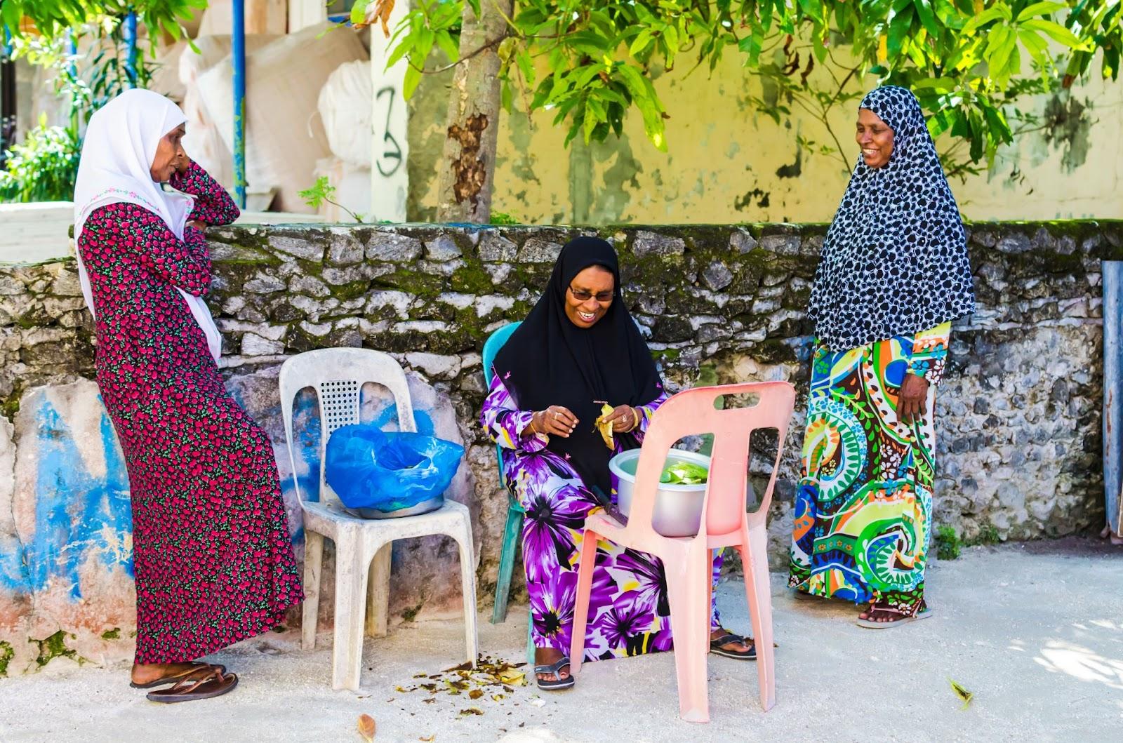 Local women in bright national clothes harvesting leaves on one of the central streets of small tropical island, Kaafu Atoll, Kuda Huraa Island, Maldives