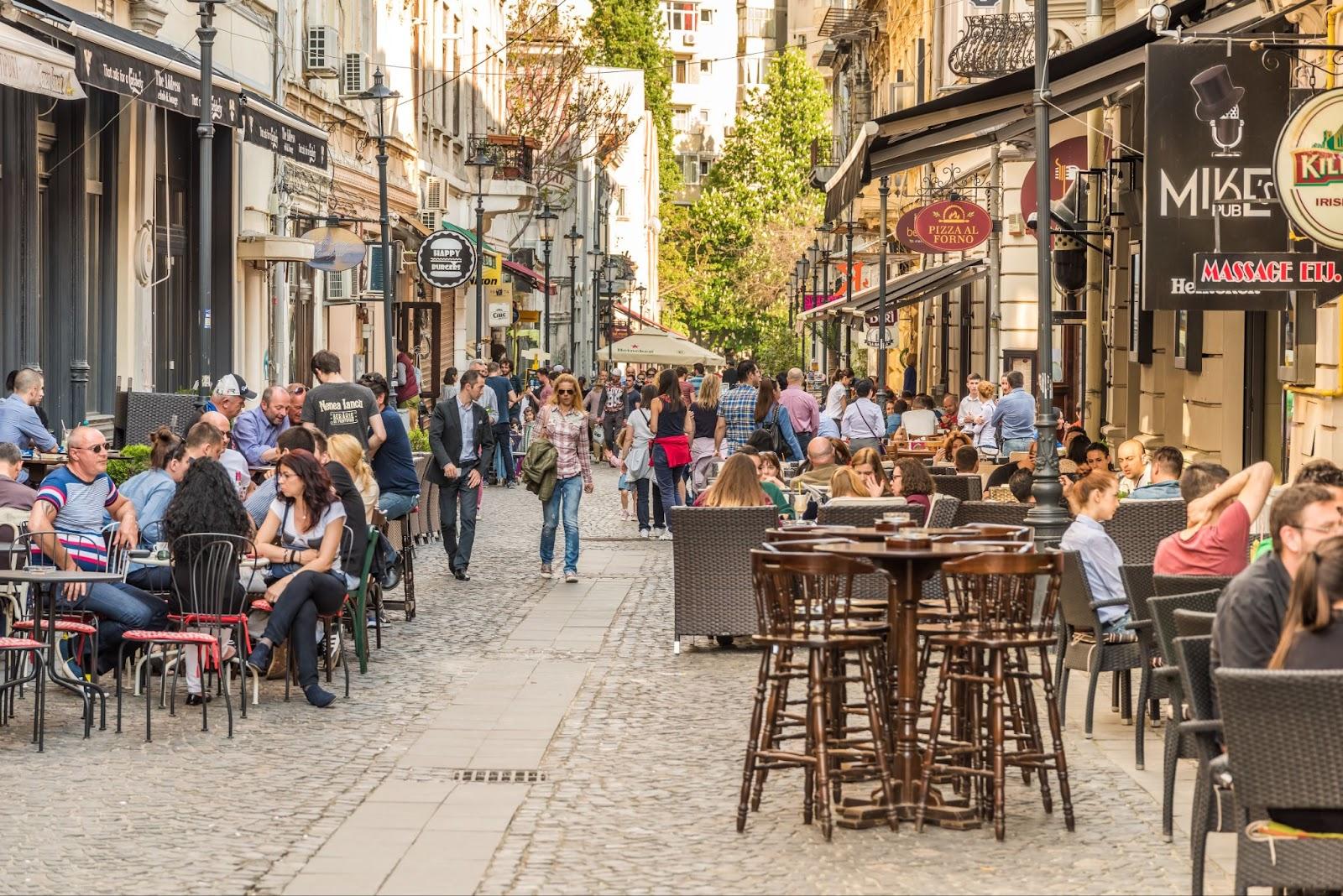 Tourists Visiting And Having Lunch At Outdoor Restaurant Cafe Downtown Lipscani Street, one of the most busiest streets of central Bucharest.