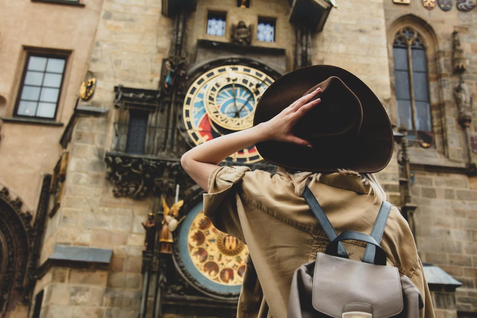 Blonde woman with hat and backback near famous clock in Prague, Czech Republic