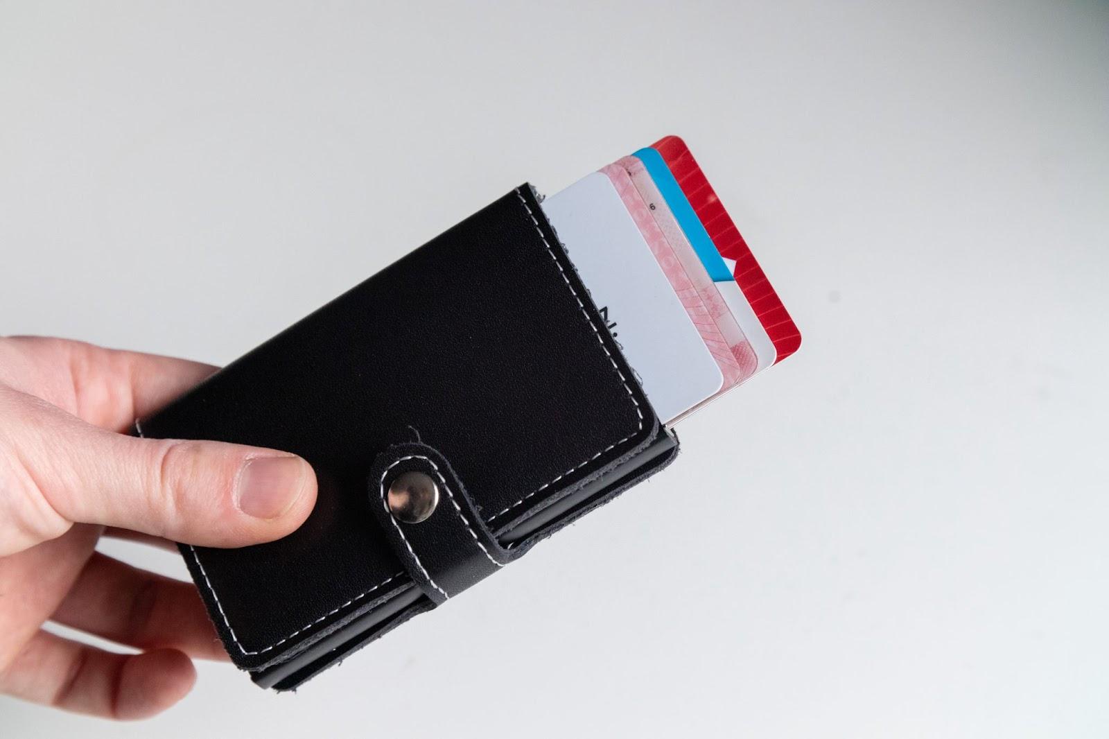 Close up man's hand holding black leather wallet ejecting credit cards on isolated white background. Fashionable, slim wallet.