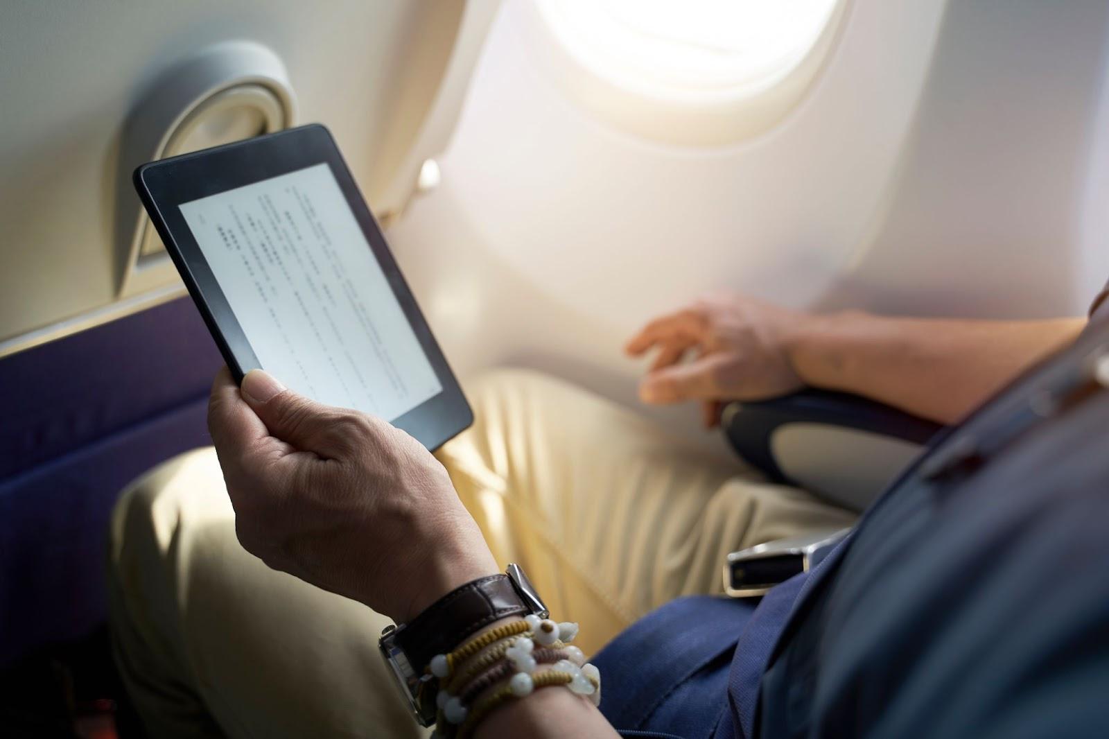 asian man male passenger sitting in cabin of airplane reading ebook using e-reader