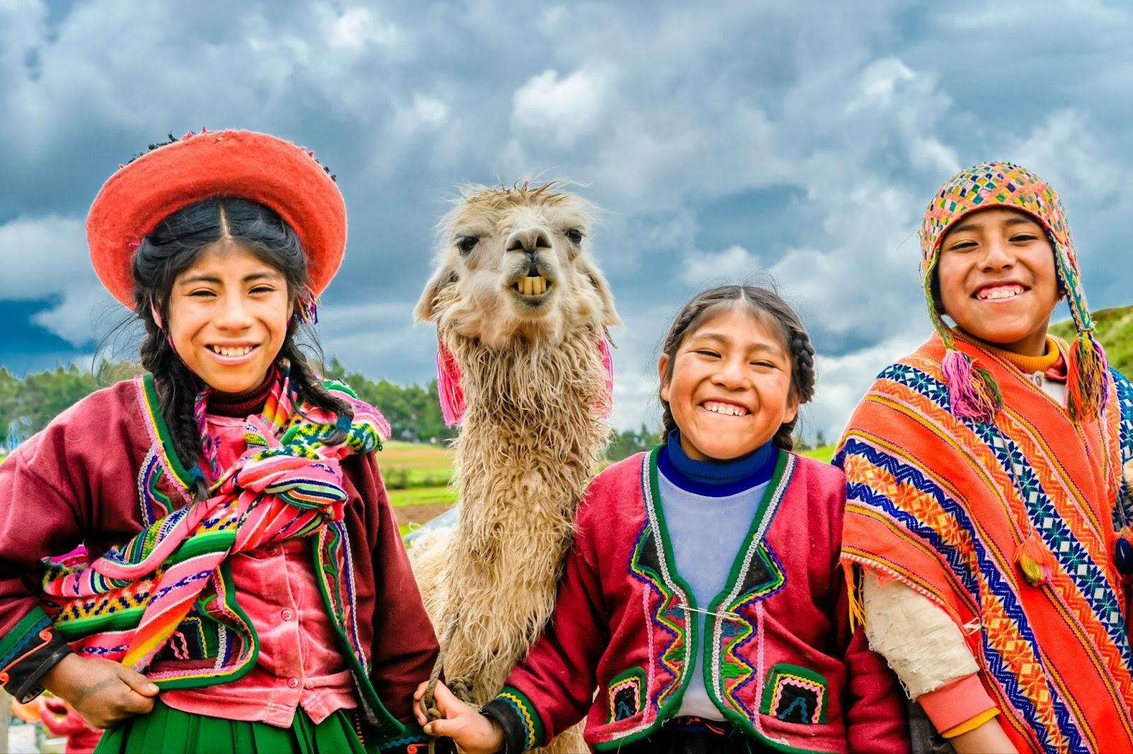 3 children in traditional peruvian dress with an Alpaca