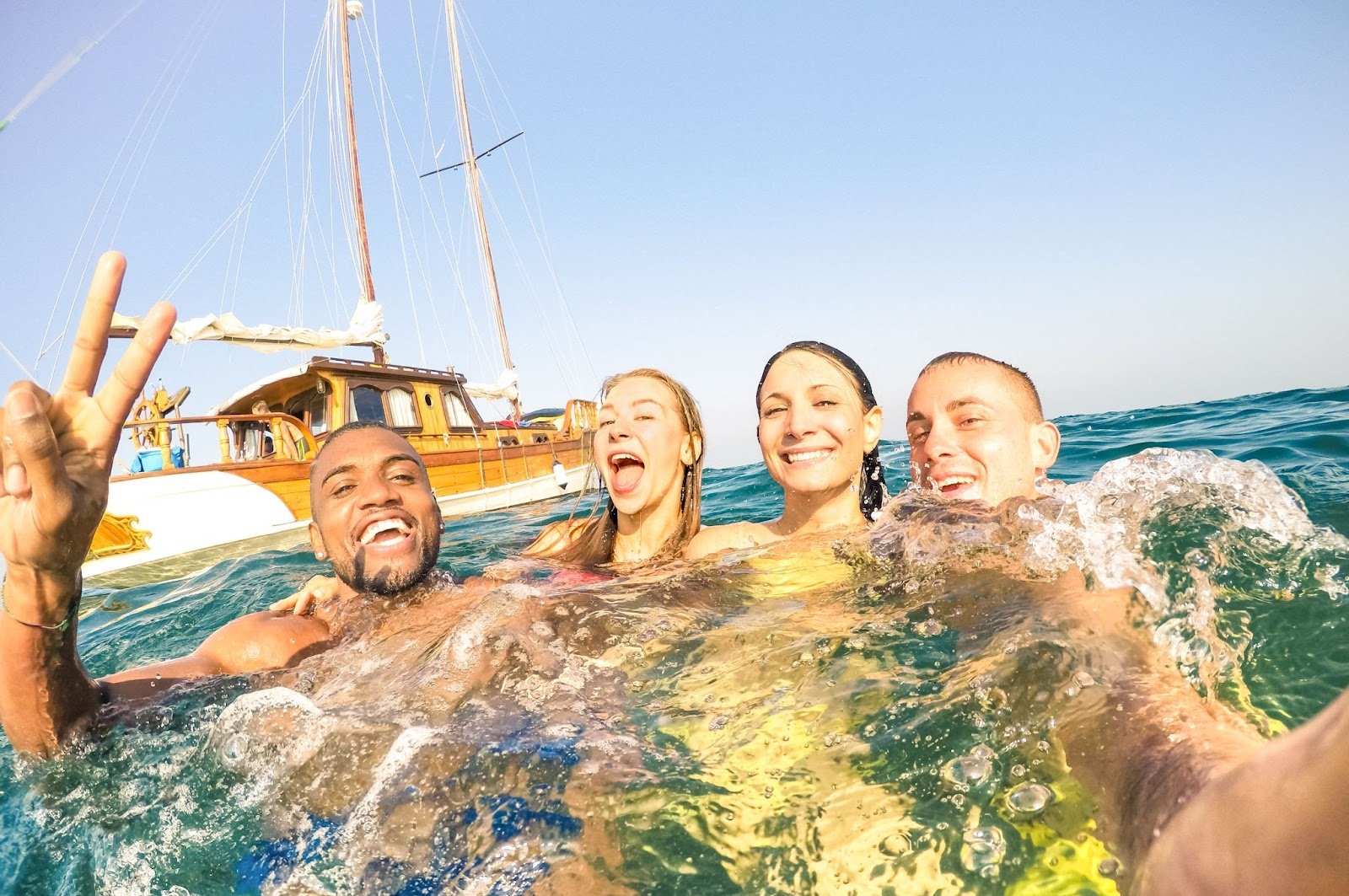Young multiracial friends taking selfie and swimming on sailing boat sea trip