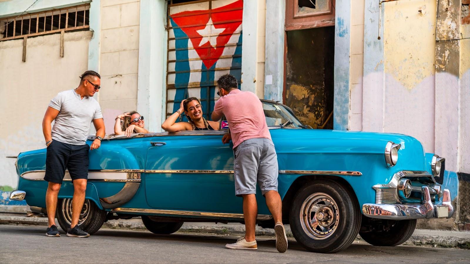 Group of multicultural friends having fun in Havana with American cars. 