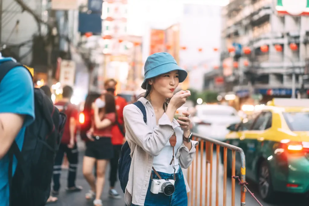 Happy young adult asian foodie woman backpack traveller eating asia dessert. People traveling with lifestyle outdoor at China town street food market. Bangkok, Thailand