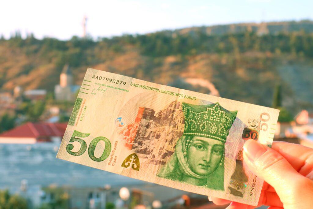 50 Georgian Lari Banknotes in Obverse Side in Hand with Blurry Tbilisi City View in Backdrop
