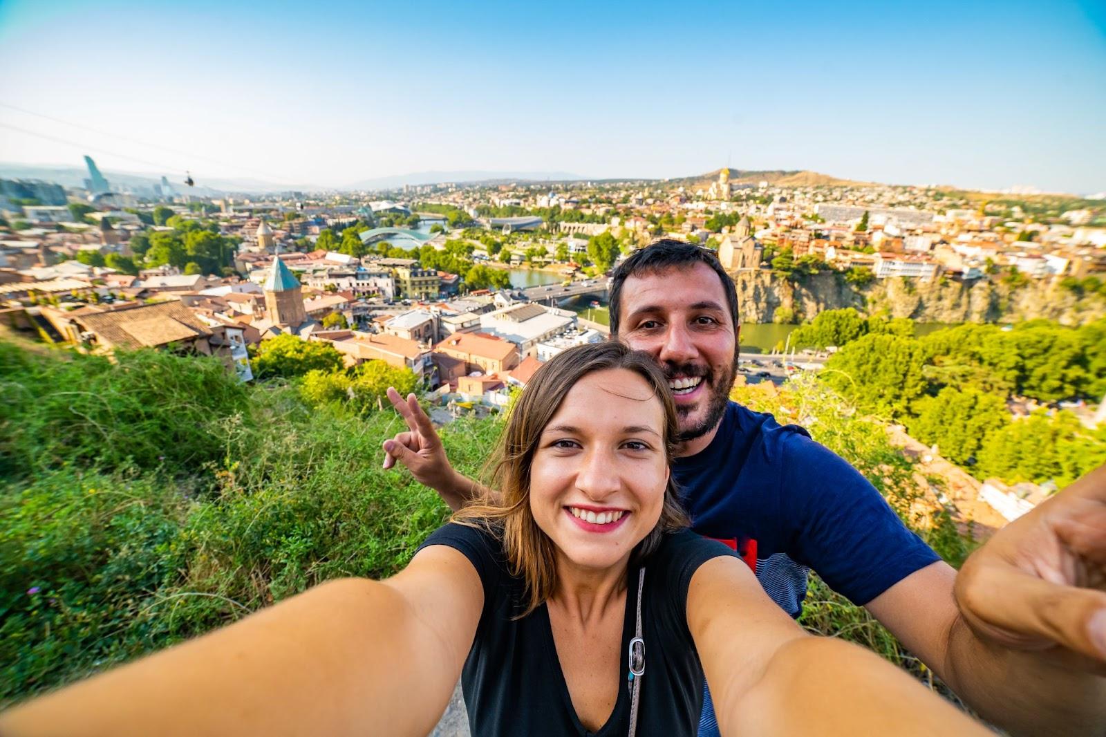 Couple taking selfie in Tbilisi with aerial view of old Tbilisi. They got their travel money and best exchange rate at Manor FX