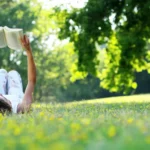 Young woman lying and reading her favorite book on a o green meadow covered with yellow flowers in a nice sunny summer/spring day.Concept of recreation, education and study , curiosity, leisure time