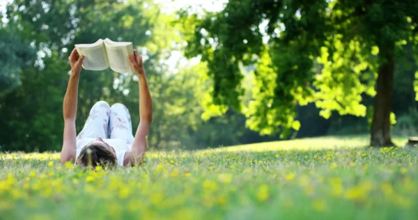 Young woman lying and reading her favorite book on a o green meadow covered with yellow flowers in a nice sunny summer/spring day.Concept of recreation, education and study , curiosity, leisure time