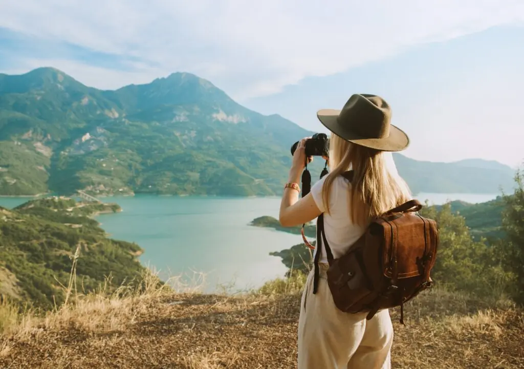 Woman photographer with big backpack taking photo of mountains and blue lake. Travel and hobby concept