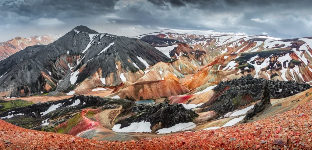 Amazing Icelandic landscape of colorful rainbow volcanic Landmannalaugar mountains, at famous Laugavegur hiking trail with dramatic snowy sky, and red volcano soil in Iceland.