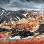 Amazing Icelandic landscape of colorful rainbow volcanic Landmannalaugar mountains, at famous Laugavegur hiking trail with dramatic snowy sky, and red volcano soil in Iceland.