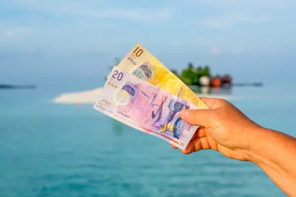 Tourist holding Maldivian notes in front of background of island in ocean